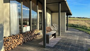A covered outdoor area with a bench, a stack of firewood, and a view of a field.