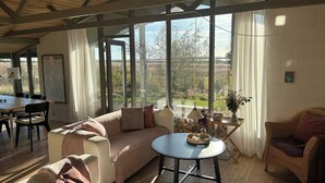 A spacious living area with a large window, a sofa, a round table, and a wicker chair.