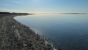 A calm body of water with a pebbly shore and distant land.