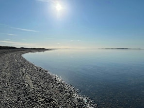 A calm body of water with a pebbly shore and distant land. - Summer house with fields and fjord views (Thyholm)