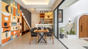 A modern dining area with a wooden table and chairs, a staircase with a geometric wall design, and a stone wall with plants. - Alisa 3 Villa (Kerobokan)