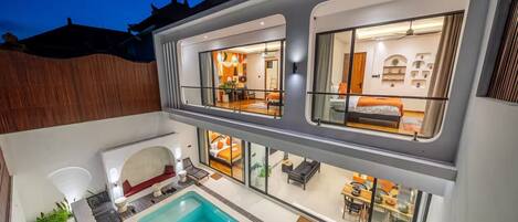 Ein modernes, zweistöckiges Gebäude mit Swimmingpool, mehreren Zimmern mit großen Fenstern und einem Balkon.