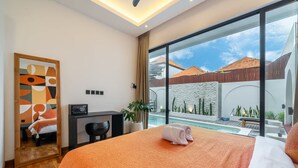 A hotel room with a bed, a desk, a chair, a large window, and a view of the outside. - Alisa 3 Villa (Kerobokan)