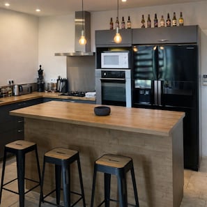 Eine moderne Küche mit einer zentralen Kochinsel, Barhocker, einer Mikrowelle, einem Backofen und einem Kühlschrank.
