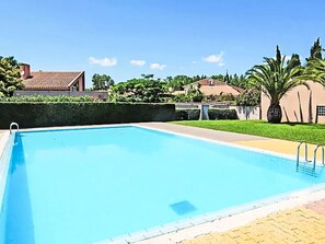 Ein rechteckiger Pool mit glasklar blauem Wasser, umgeben von einer gepflasterten Liegefläche.