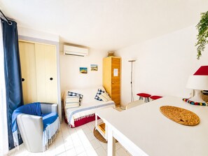Ein kleines Zimmer mit einem Bett, einem Sessel, einem kleinen Tisch, einem Schrank und einer Stehlampe.