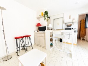 Eine kompakte Küche mit Essbereich, einem kleinen Barhocker-Set, einer Stehlampe und einem Fernseher.