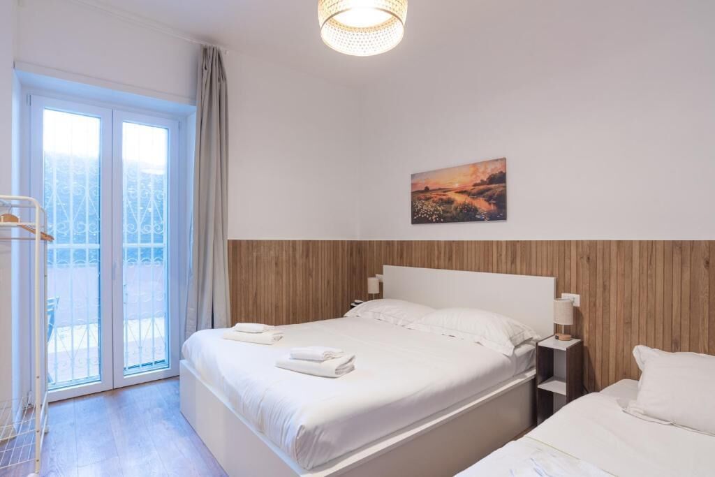Ein Hotelzimmer mit Bett, Nachttisch, Vorhängen am Fenster und einem Bild an der Wand.