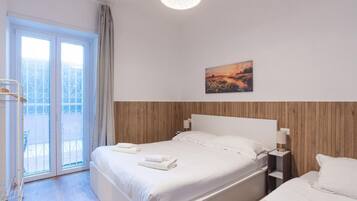 Ein Hotelzimmer mit Bett, Nachttisch, Vorhängen am Fenster und einem Bild an der Wand.