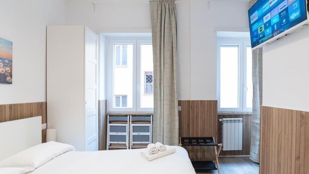 A hotel room with a bed, a TV mounted on the wall, a window with curtains, and a radiator.