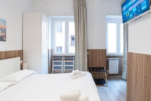 A hotel room with a bed, a TV mounted on the wall, a window with curtains, and a radiator. - Residence San Paolo (Rome)