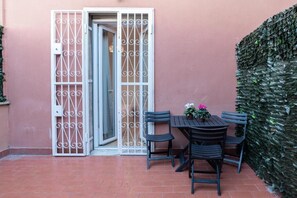 A patio with a table and chairs, a white gate, and a green hedge.