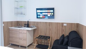 A modern kitchen with a built-in sink, wooden cabinets, a small shelf, and a wall-mounted digital screen displaying various apps.