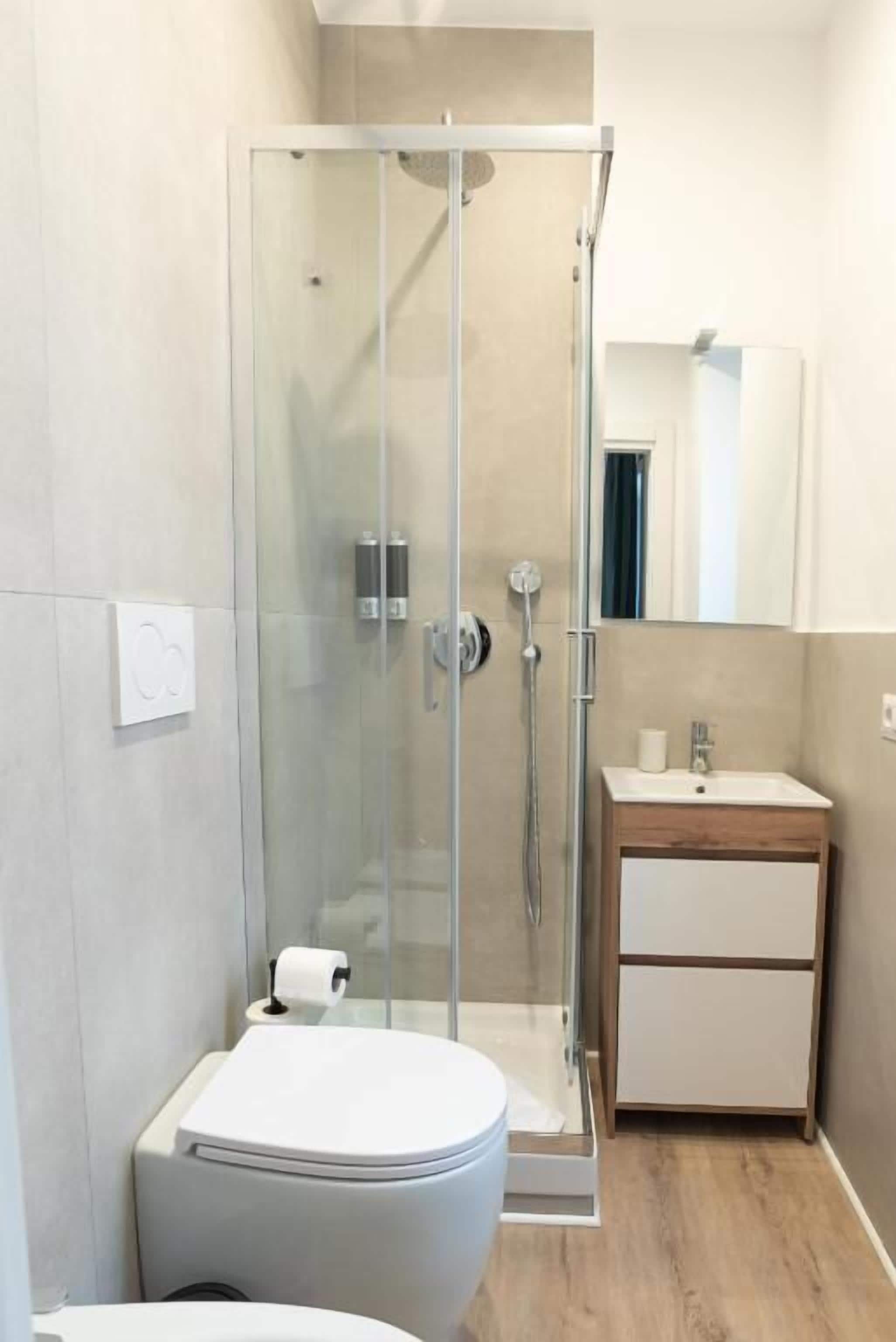 A modern bathroom with a glass-enclosed shower, a toilet, a sink with a mirror, and a wooden cabinet.