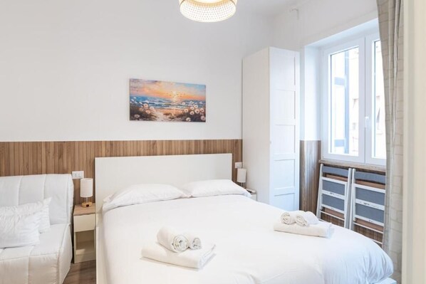A hotel room with a bed, a nightstand, a lamp, a painting on the wall, and a window with a view.