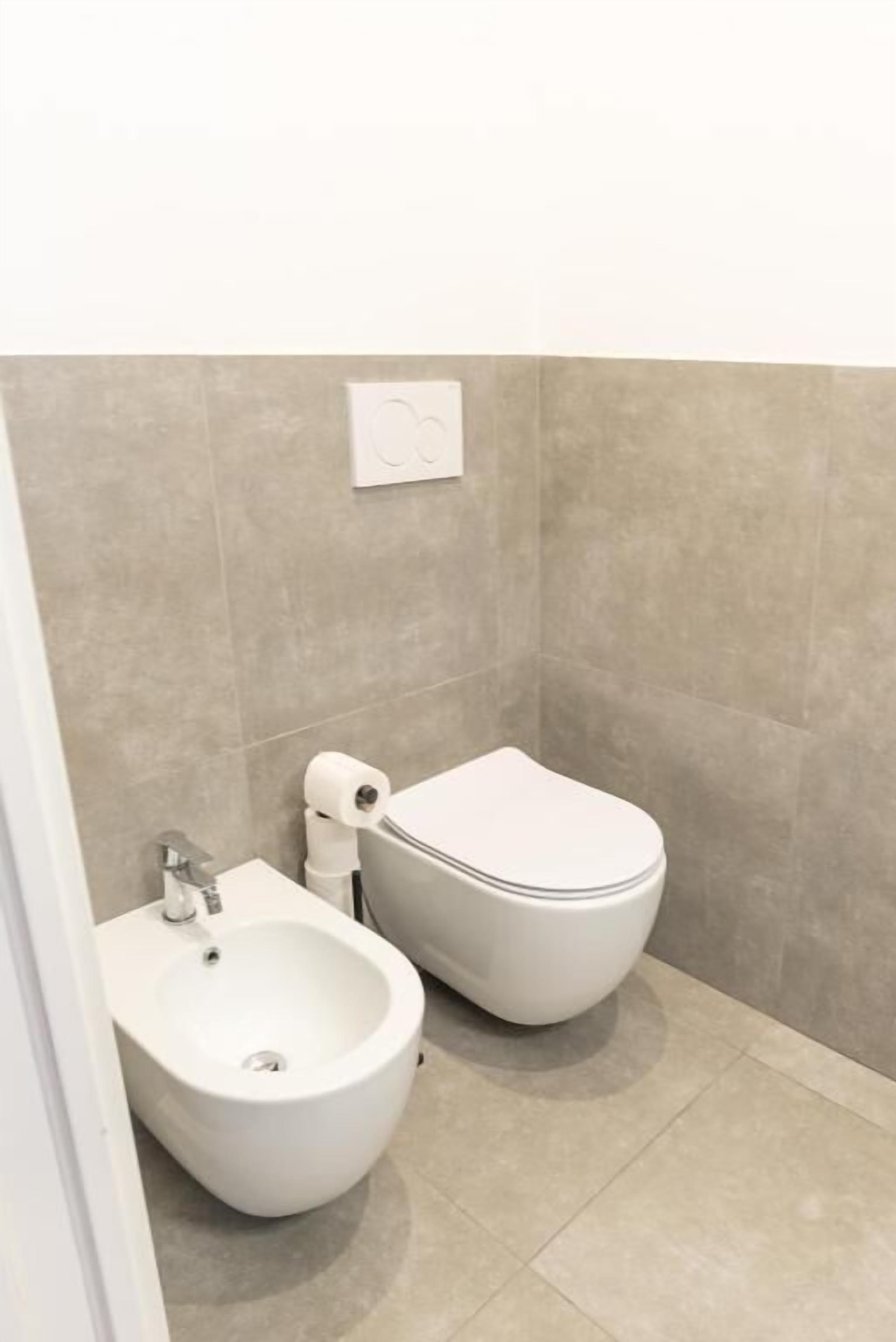 A small bathroom with a bidet, toilet, and a towel dispenser.