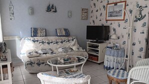 Una sala de estar con sofá, televisión, sillas de mimbre y un papel tapiz estampado.