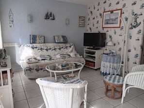 Ein Wohnzimmer mit einer Couch, Fernseher, Korbstühlen und einer Wand mit Muster.