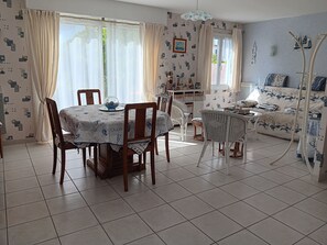 Ein Essbereich mit einem Tisch für vier Personen, umgeben von Stühlen, und eine Couch im Hintergrund.