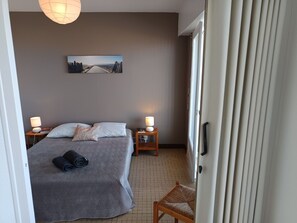 Ein Hotelzimmer mit einem Bett, zwei Nachttischen mit Lampen, einem Gemälde an der Wand und einem Fenster mit Vorhängen.