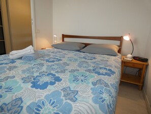 Ein Schlafzimmer mit einem Bett, Kissen, einem Nachttisch mit Lampe und einem gefalteten Handtuch auf dem Bett.