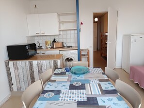 Eine kompakte Küche mit Waschmaschine, Mikrowelle und Toaster. Ein Esstisch mit Stühlen und einem gemusterten Tischläufer.