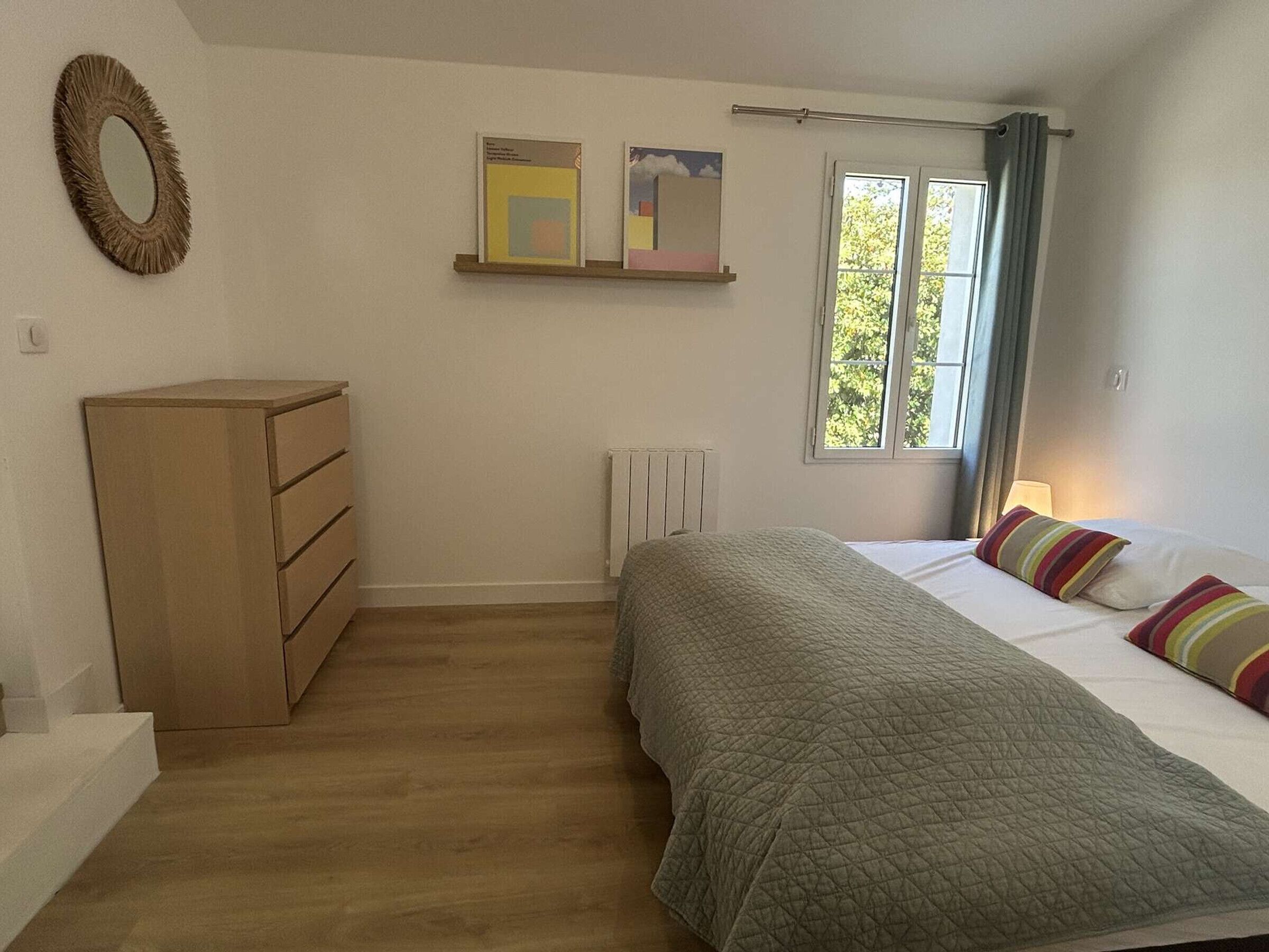 Un dormitorio con cama, cómoda, radiador y ventana con cortinas.