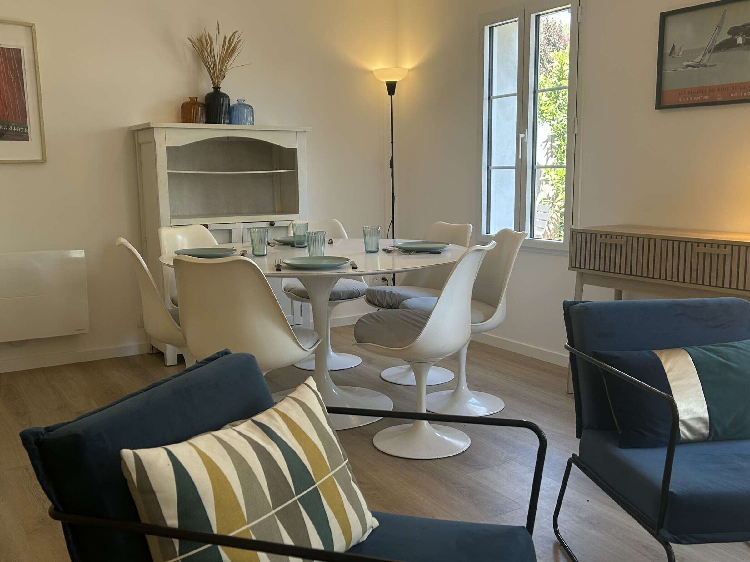 Un coin repas comprenant une table et des chaises, un radiateur, une lampe sur pied et une fenêtre donnant sur un paysage agréable.