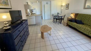Ett kompakt bostadsutrymme med ett litet kök, en matplats, en soffa och en tv.
