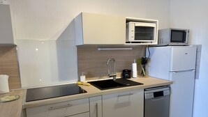 Ett kompakt kök med diskho, mikrovågsugn, kylskåp och diskmaskin.