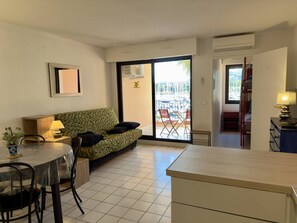 Ein kompakter Wohnbereich mit einer Couch, Esstisch, Stühlen, einer kleinen Küchenzeile und einer Glastür zum Außenbalkon mit Sitzgelegenheiten.