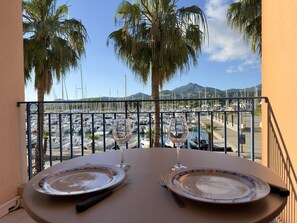 Ein Balkontisch mit zwei Tellern, zwei Weingläsern und Blick auf einen Yachthafen mit Booten und Palmen.