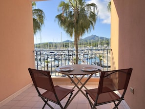 Un balcó amb taula i cadires, amb vista a una marina plena de vaixells i una muntanya al fons.