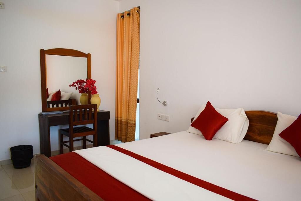 Une chambre d’hôtel avec un lit, un bureau et une chaise, un miroir et une fenêtre avec des rideaux.