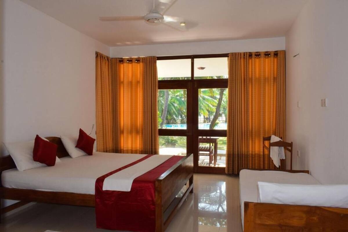 A hotel room with a bed, a chair, a table, and a view of palm trees through the window.