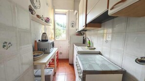 Una cocina compacta con azulejos blancos, microondas, hervidor de agua y ventana que proporciona luz natural.