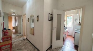 Un pasillo con una silla roja, un espejo y una puerta que da a una zona de cocina.