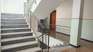 Una escalera con barandillas de metal, piso de baldosas y un pasillo con una puerta.