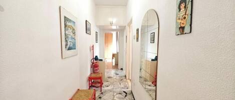 A narrow hallway with a red chair, a mirror, and framed pictures on the walls.