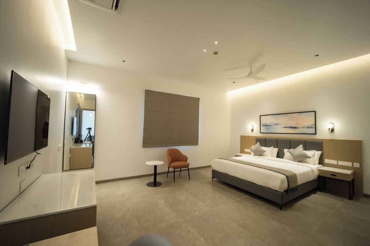 A modern hotel room with a large bed, a TV, a chair, and a desk.