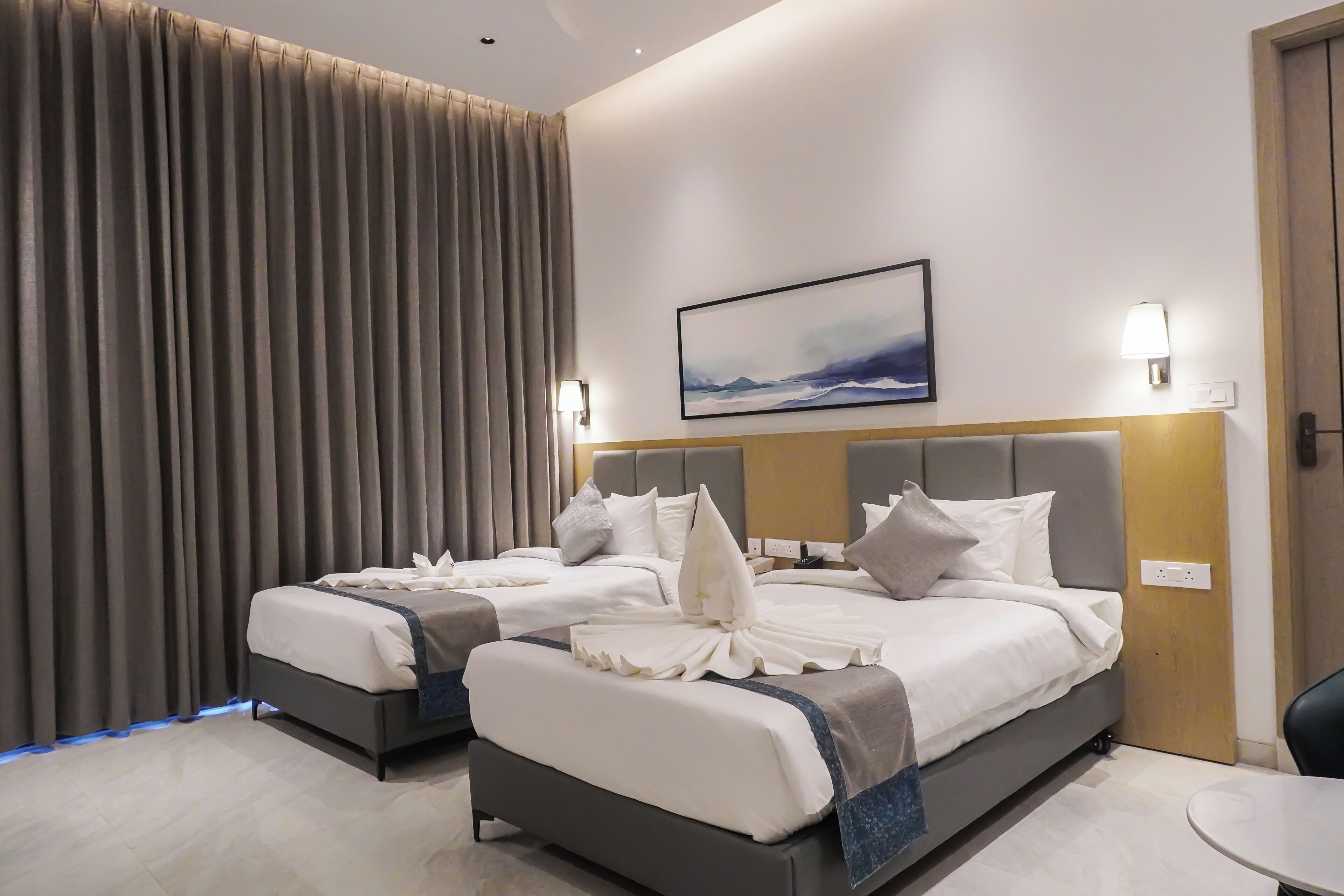 A hotel room with two beds, a painting on the wall, and a lamp.