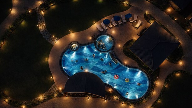 An aerial view of a swimming pool area with multiple pools, lounge chairs, and a well-lit pathway. - Lore Resorts and conventions (Maheshwaram)