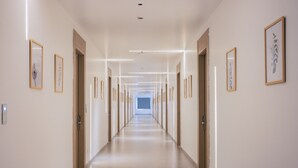 A long, well-lit hallway with framed artwork on the walls, doors on both sides, and a light-colored floor. - Lore Resorts and conventions (Maheshwaram)