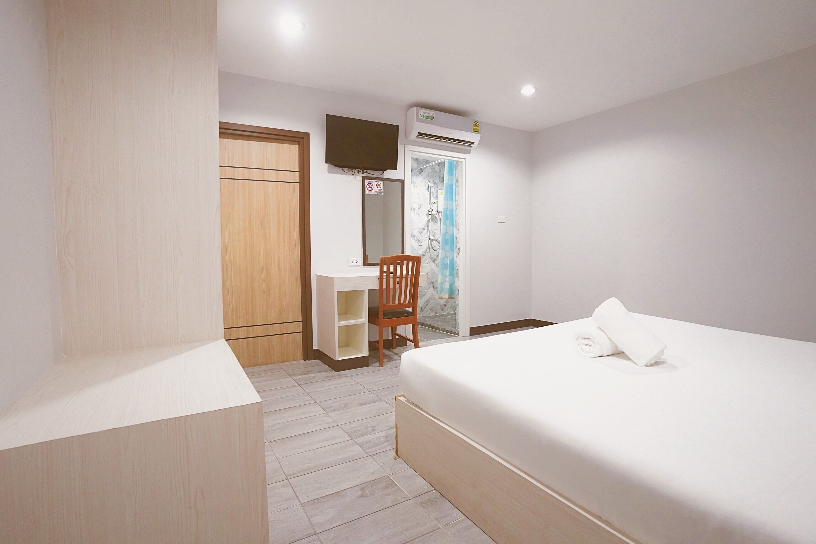 A bedroom with a bed, a desk, a chair, a wardrobe, and an air conditioning unit.