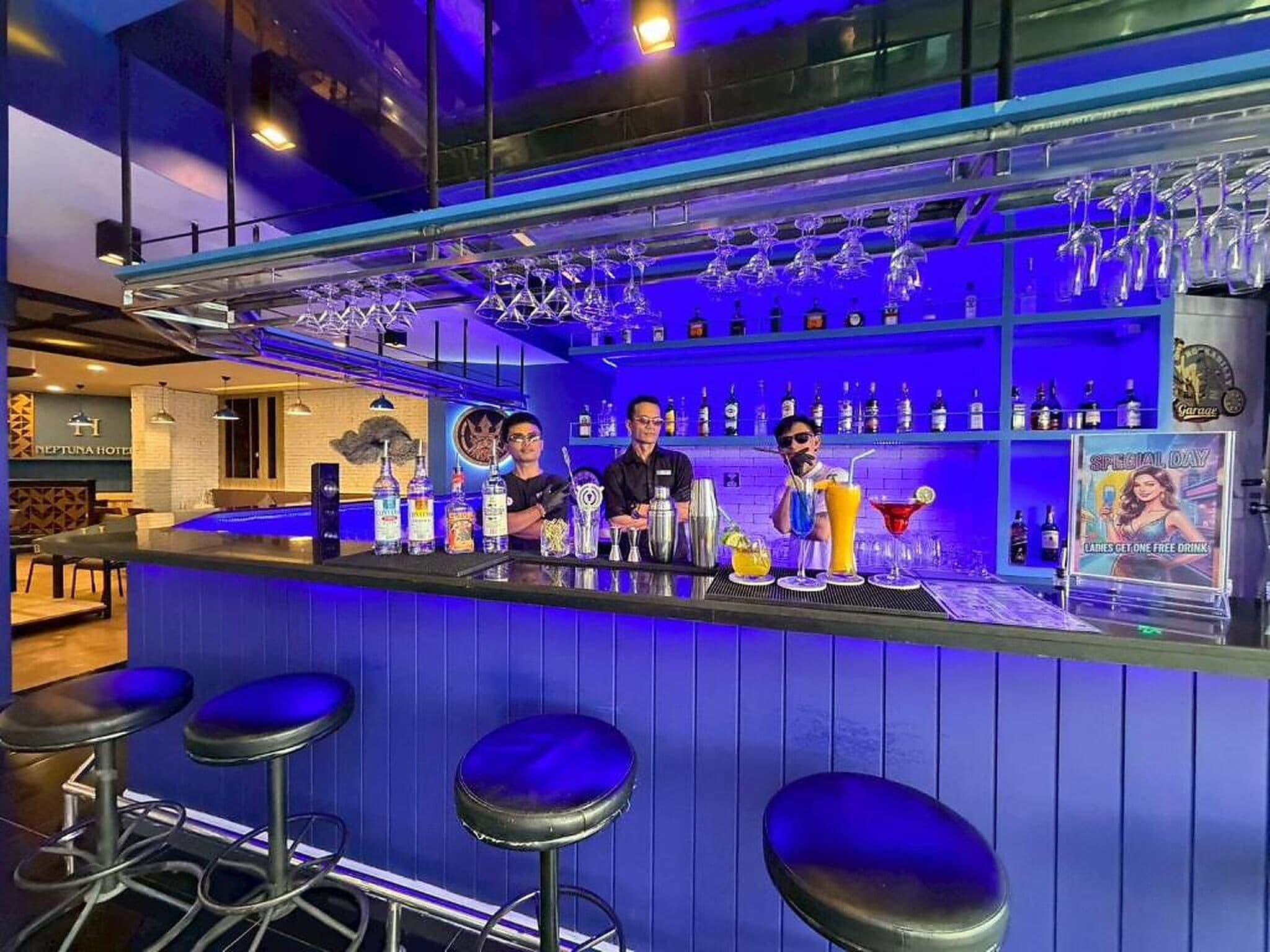 Un espace bar avec des tabourets, un barman et une étagère remplie de bouteilles.