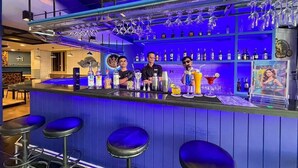 En bar med barstole, en bartender og en hylde med flasker.