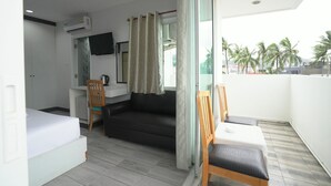Une chambre comprenant un lit, un canapé, une petite table, une chaise, un téléviseur et un balcon avec vue sur les palmiers.