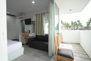 A room with a bed, a sofa, a small table, a chair, a TV, and a balcony with a view of palm trees. - Blue Neptuna Hotel Patong by Koko (Patong)