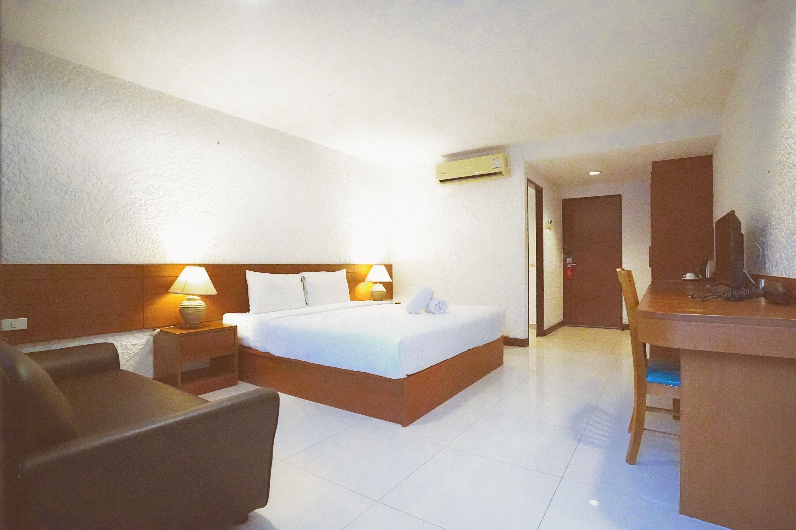 Una habitación de hotel con cama, escritorio, silla, lámpara y aire acondicionado.