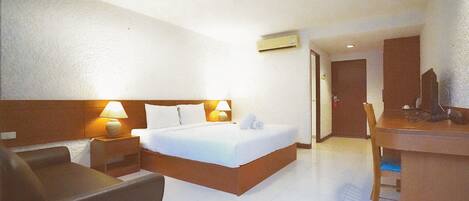 Una habitación de hotel con cama, escritorio, silla, lámpara y aire acondicionado.